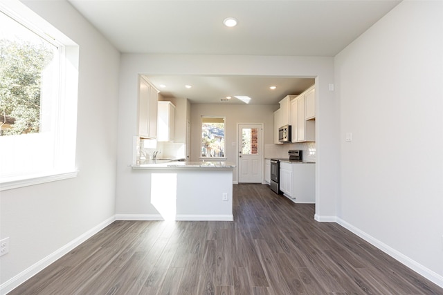 kitchen with dark hardwood / wood-style floors, kitchen peninsula, decorative backsplash, white cabinets, and appliances with stainless steel finishes