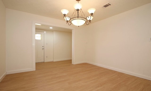 spare room with an inviting chandelier and light hardwood / wood-style flooring