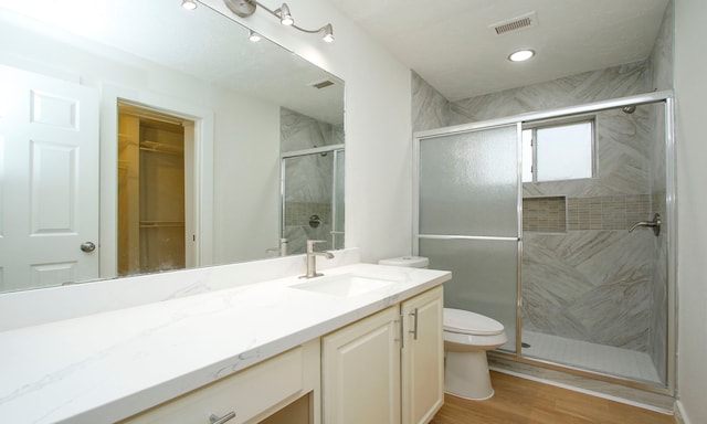 bathroom featuring hardwood / wood-style floors, walk in shower, vanity, and toilet