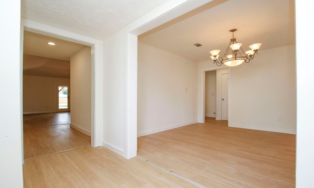 spare room with light hardwood / wood-style flooring, a textured ceiling, and an inviting chandelier