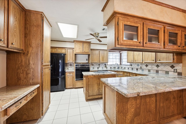 kitchen with light tile patterned flooring, kitchen peninsula, black appliances, light stone countertops, and ceiling fan