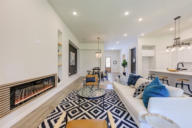 living room featuring an inviting chandelier, light hardwood / wood-style flooring, built in features, and sink