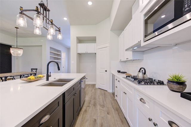 kitchen with light wood-type flooring, sink, white cabinets, stainless steel appliances, and decorative light fixtures