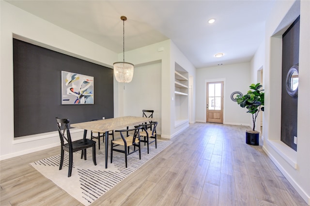 dining area with a notable chandelier, built in shelves, and light hardwood / wood-style floors