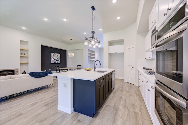 kitchen with an island with sink, white cabinets, light hardwood / wood-style flooring, decorative light fixtures, and sink