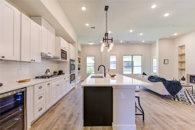 kitchen with white cabinets, wine cooler, light wood-type flooring, and sink