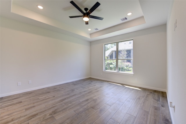 empty room featuring light hardwood / wood-style flooring, a tray ceiling, and ceiling fan