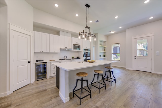 kitchen featuring white cabinets, wine cooler, a center island with sink, stainless steel appliances, and light hardwood / wood-style floors