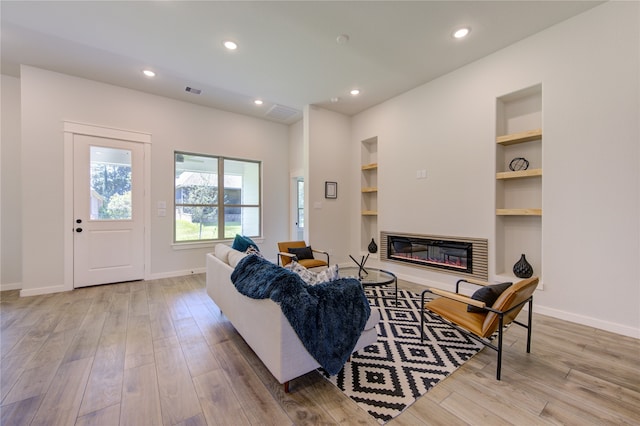 living room with built in shelves and light hardwood / wood-style flooring