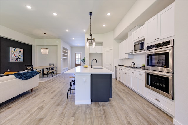 kitchen featuring an island with sink, stainless steel appliances, hanging light fixtures, and sink