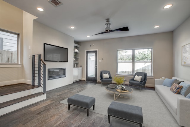 living room with built in shelves, ceiling fan, and dark hardwood / wood-style floors