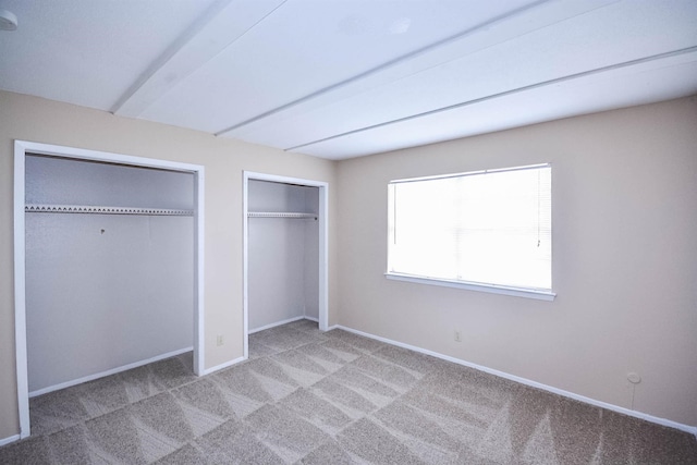 unfurnished bedroom featuring light carpet, multiple closets, and beamed ceiling