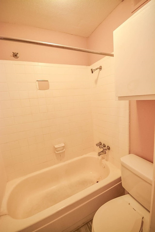 bathroom with a textured ceiling, tiled shower / bath combo, and toilet