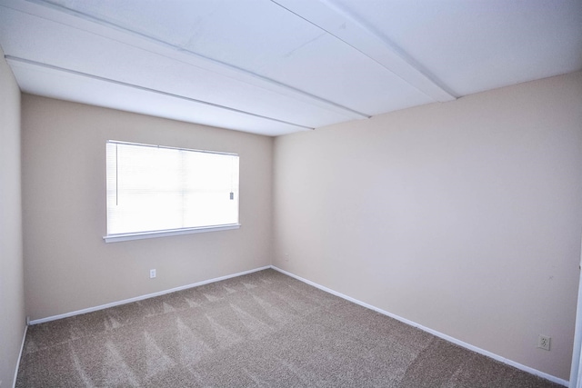 carpeted spare room featuring beamed ceiling