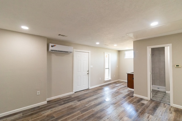 basement with a textured ceiling, dark wood-type flooring, and a wall mounted AC