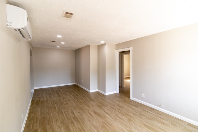 unfurnished room featuring a textured ceiling, a wall mounted AC, and light hardwood / wood-style flooring