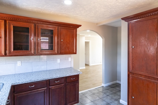 kitchen featuring a textured ceiling, hardwood / wood-style flooring, light stone counters, and tasteful backsplash