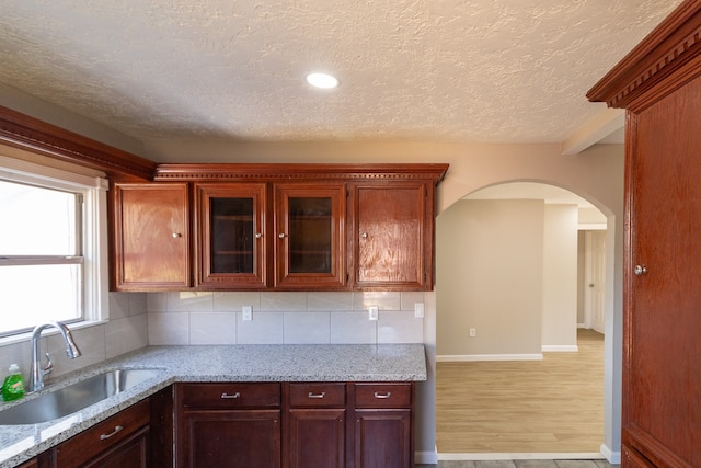 kitchen with backsplash, light hardwood / wood-style floors, sink, and light stone counters