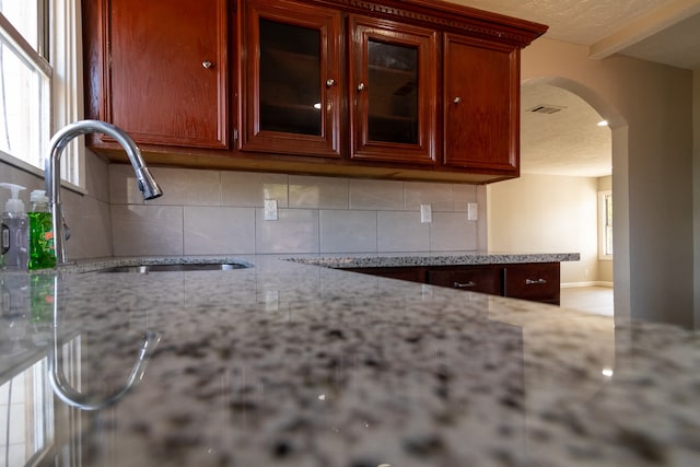 kitchen with backsplash, light stone countertops, beamed ceiling, and sink