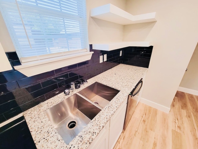 kitchen with decorative backsplash, white cabinets, light stone countertops, light hardwood / wood-style flooring, and sink