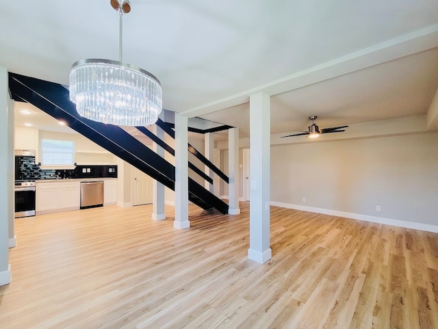 unfurnished living room with ceiling fan with notable chandelier and light hardwood / wood-style floors