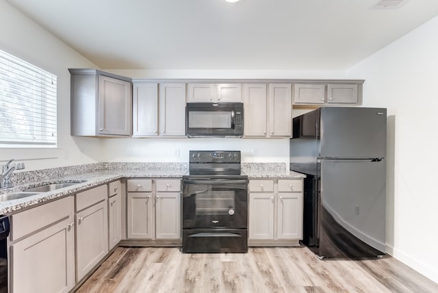 kitchen featuring light stone countertops, black appliances, light hardwood / wood-style floors, and gray cabinetry