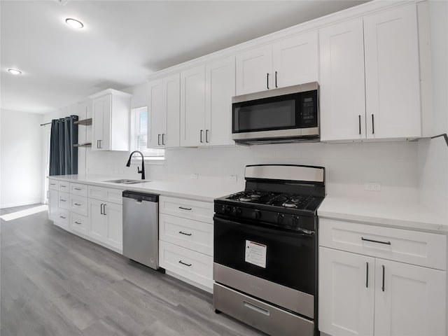 kitchen with sink, white cabinetry, stainless steel appliances, light hardwood / wood-style floors, and decorative backsplash