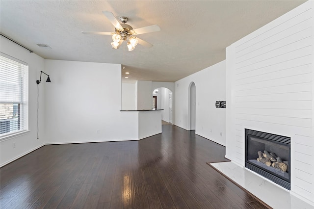 23307 W Pine Ivy Ln, Tomball, TX 77375 - unfurnished living room with arched walkways, a ceiling fan, a large fireplace, dark wood-type flooring, and baseboards