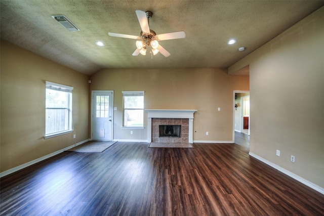 unfurnished living room featuring a textured ceiling, lofted ceiling, a tiled fireplace, dark hardwood / wood-style flooring, and ceiling fan