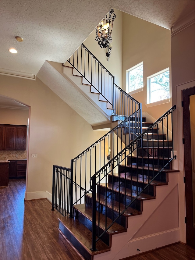 stairs featuring an inviting chandelier, wood-type flooring, a textured ceiling, and crown molding