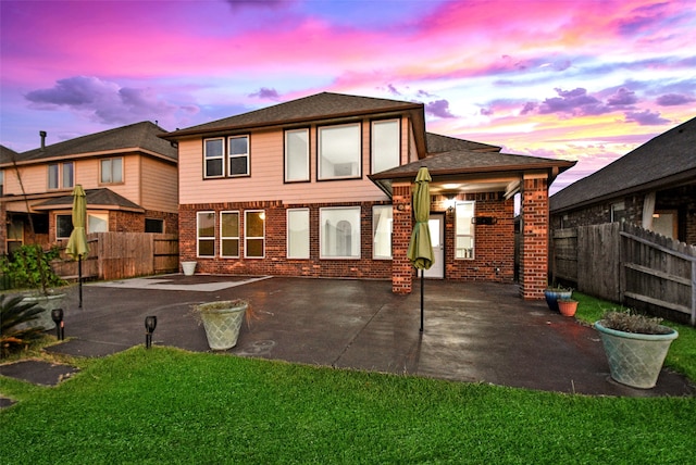 back house at dusk featuring a lawn and a patio