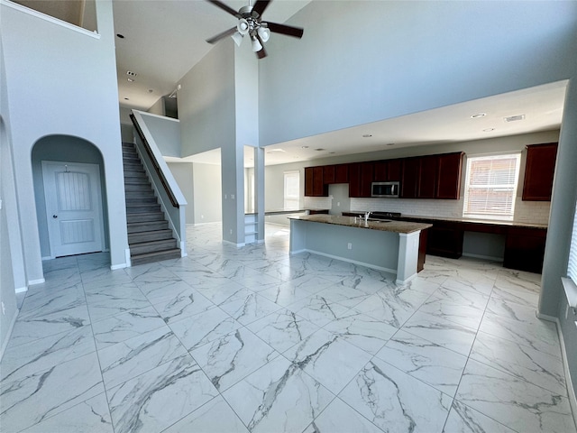 kitchen with ceiling fan, decorative backsplash, a center island, a towering ceiling, and a kitchen breakfast bar