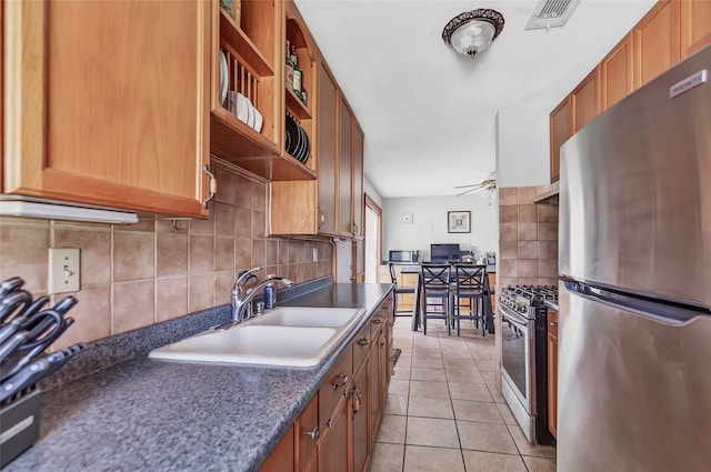 kitchen featuring decorative backsplash, light tile patterned floors, stainless steel appliances, ceiling fan, and sink