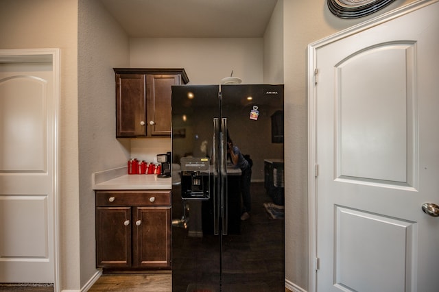 kitchen featuring dark brown cabinets, black fridge, and dark hardwood / wood-style flooring