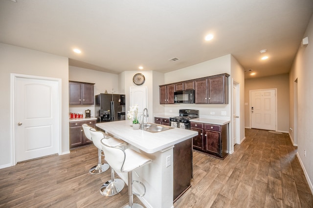 kitchen featuring dark brown cabinets, a breakfast bar, light hardwood / wood-style floors, an island with sink, and black appliances