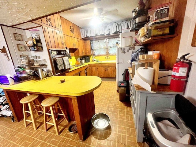 kitchen featuring ceiling fan, kitchen peninsula, wooden walls, black oven, and a kitchen bar