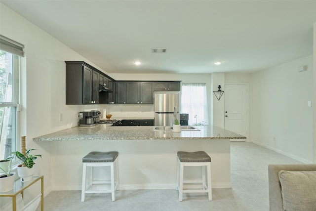 kitchen featuring light stone counters, sink, kitchen peninsula, a kitchen breakfast bar, and stainless steel appliances