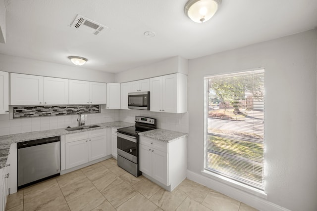 kitchen featuring sink, white cabinets, appliances with stainless steel finishes, light stone counters, and tasteful backsplash