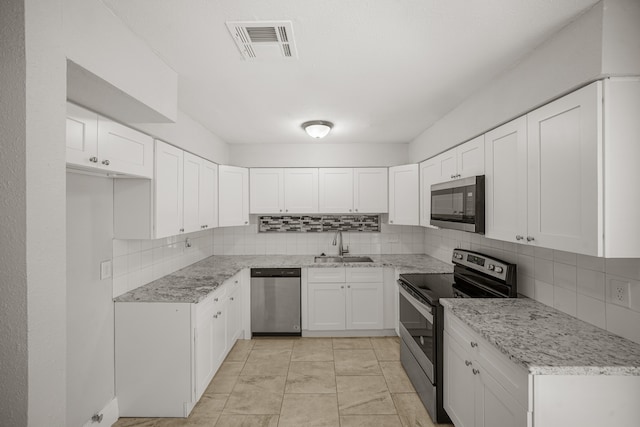 kitchen with tasteful backsplash, light stone countertops, appliances with stainless steel finishes, sink, and white cabinetry