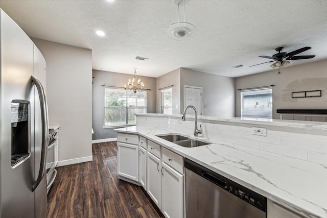 kitchen with light stone countertops, decorative light fixtures, stainless steel appliances, white cabinets, and sink