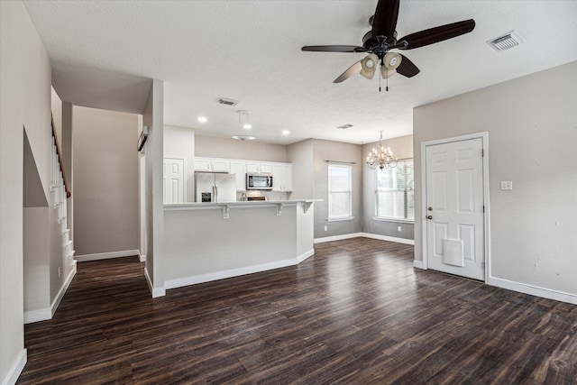 unfurnished living room with ceiling fan with notable chandelier, a textured ceiling, and dark wood-type flooring