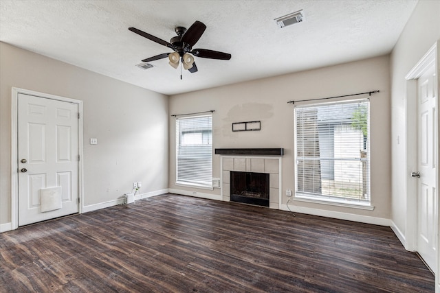 unfurnished living room featuring a tiled fireplace, dark wood-type flooring, a textured ceiling, and ceiling fan