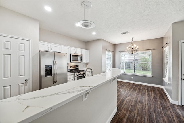 kitchen featuring stainless steel appliances, light stone countertops, hanging light fixtures, and white cabinetry