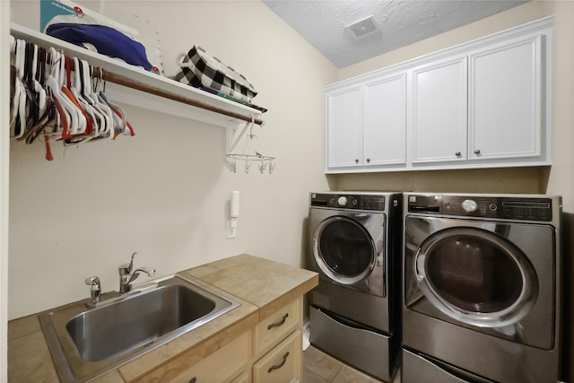 washroom featuring sink, cabinets, washing machine and dryer, a textured ceiling, and light tile patterned floors