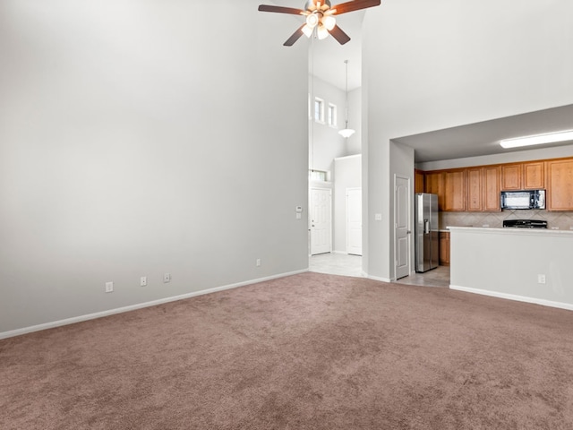 unfurnished living room featuring a towering ceiling, ceiling fan, and light colored carpet