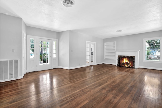 unfurnished living room with a tile fireplace, dark hardwood / wood-style flooring, built in features, and a wealth of natural light