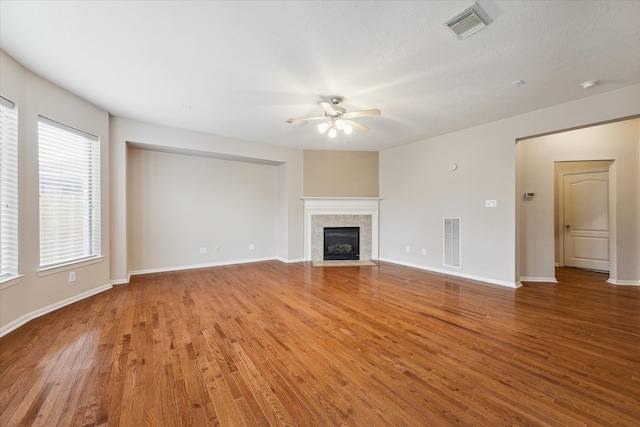 unfurnished living room with ceiling fan, a tiled fireplace, and wood-type flooring