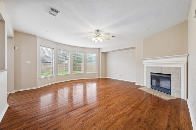 unfurnished living room featuring a textured ceiling, wood-type flooring, a tiled fireplace, and ceiling fan