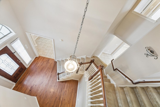 stairway featuring wood-type flooring, an inviting chandelier, a high ceiling, and a wealth of natural light