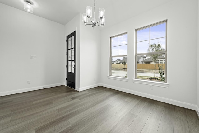 unfurnished dining area featuring a chandelier, dark wood finished floors, and baseboards